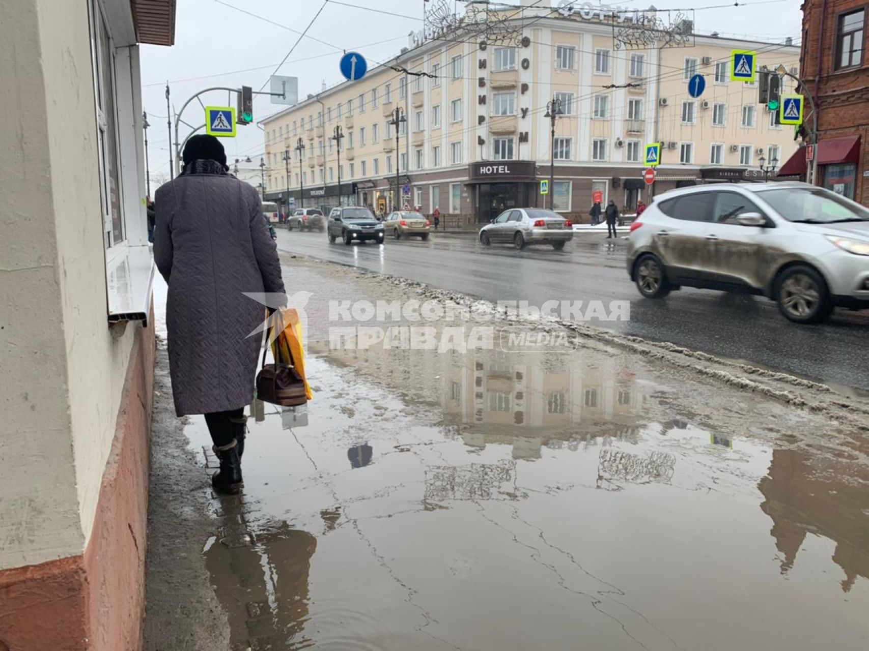 Томск. Женщина обходит большую лужу на тротуаре.