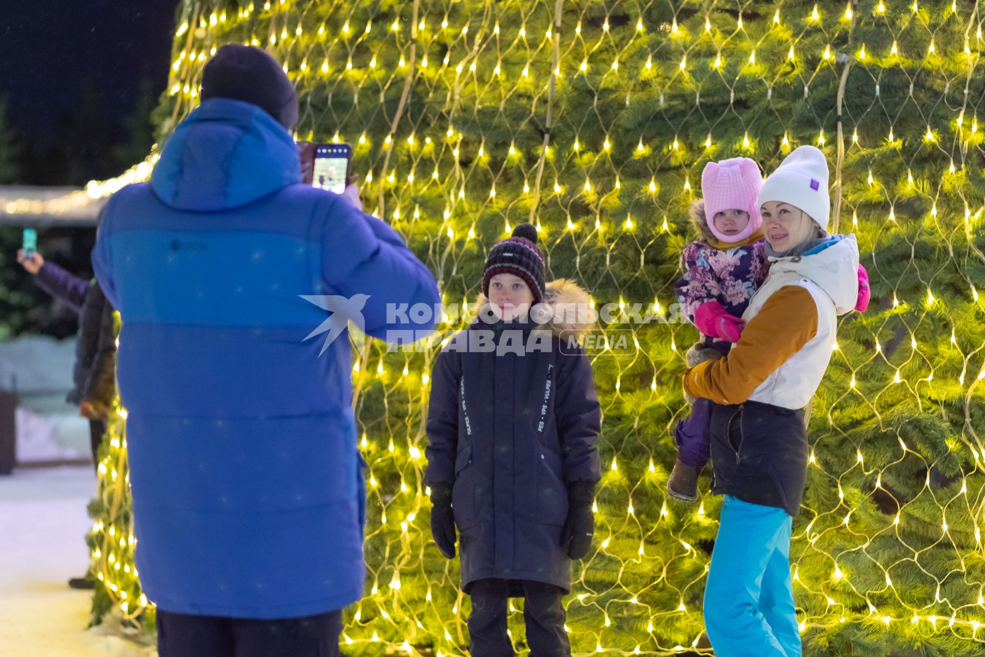 Красноярск. Мужчина и женщина с детьми фотографируются у новогодней елки.