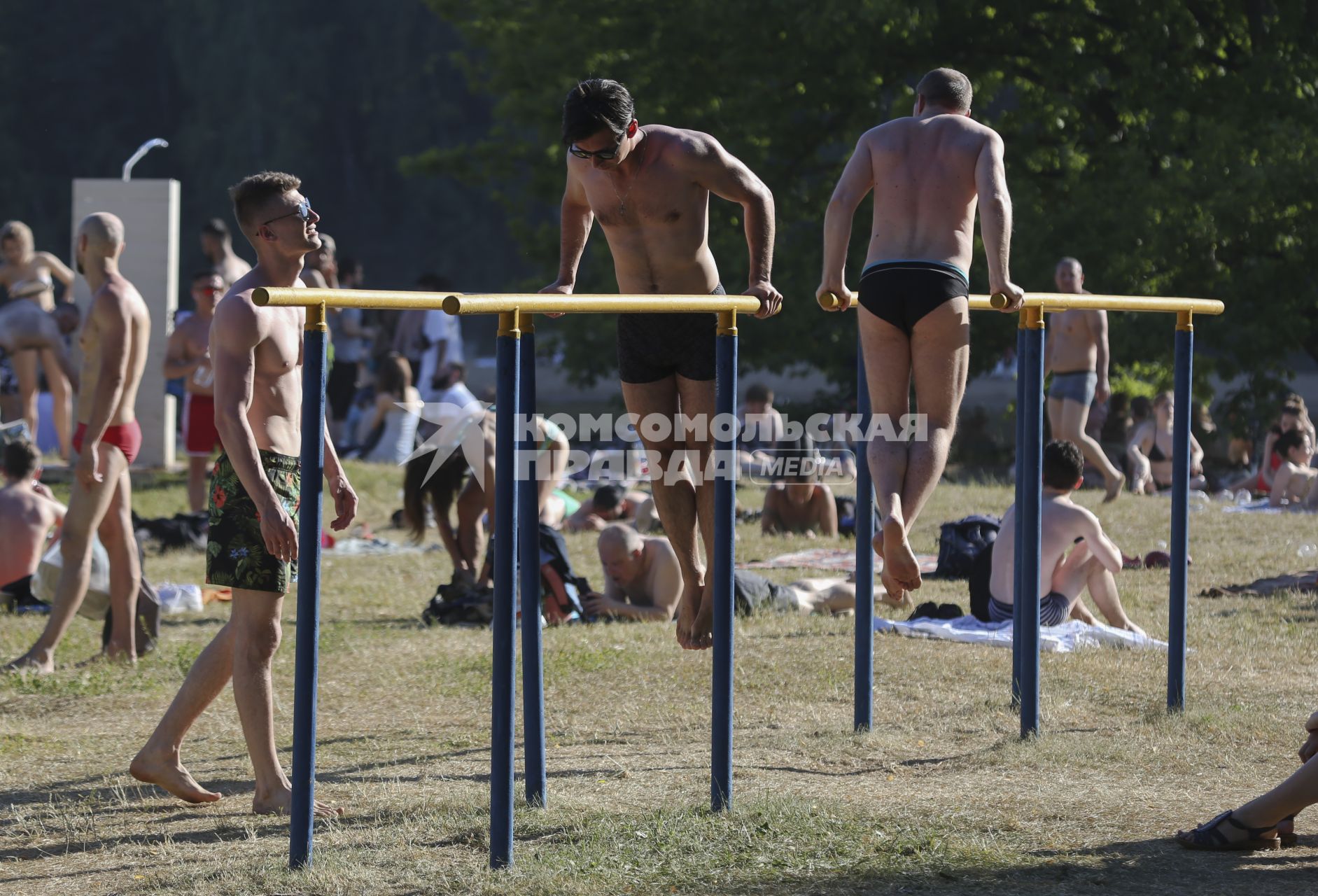 Москва.  Мужчины занимаются на брусьях на пляже.
