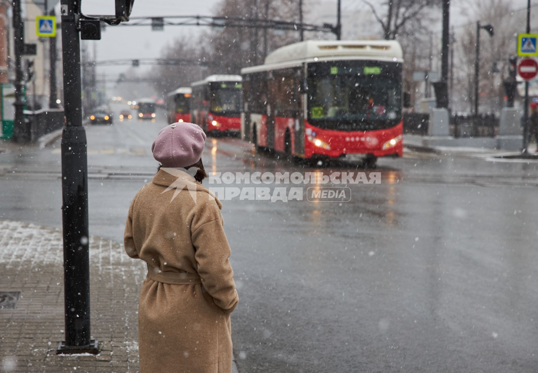 Пермь. Девушка стоит на тротуаре и смотрит на проезжающие автобусы.