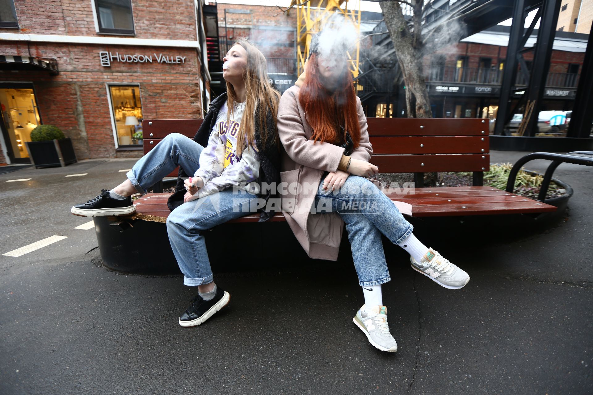 Москва. Девушки сидят на скамейке и курят вейпы.