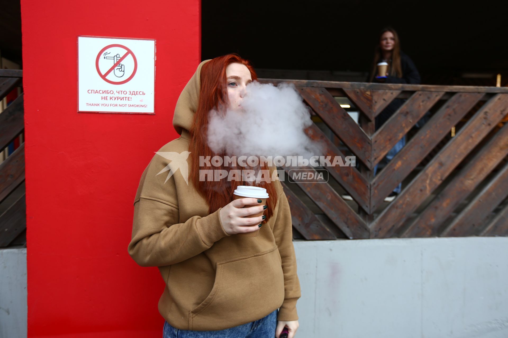 Москва. Девушка курит вейп рядом с табличкой `Спасибо, что здесь не курите!`.