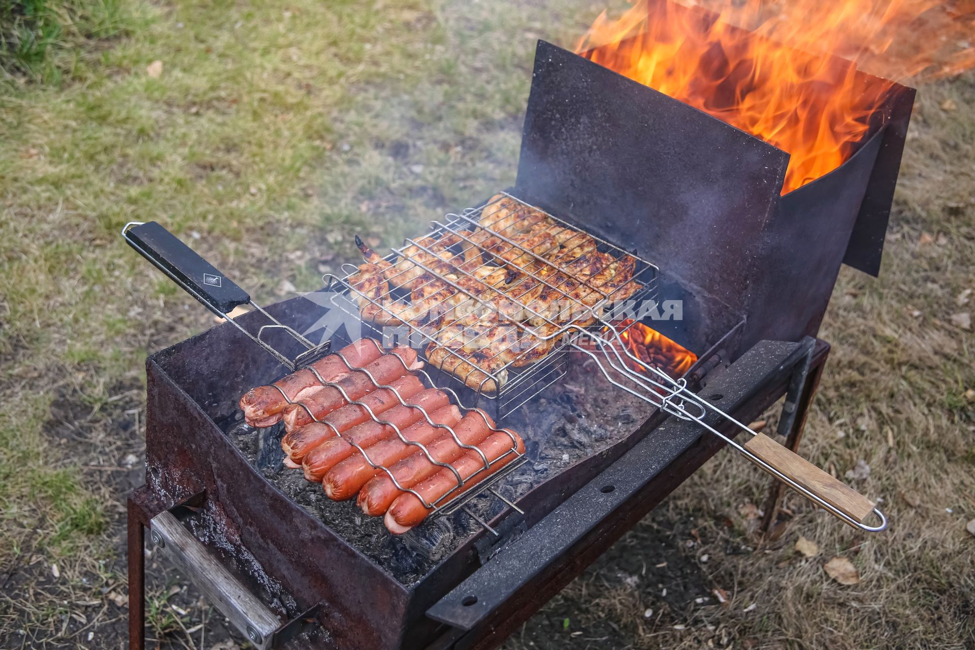 Красноярск. Приготовление куриных крылышек и сосисок на решетке на приусадебном участке.