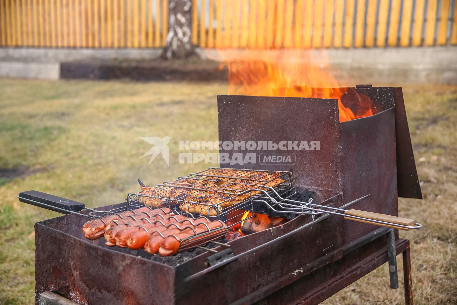 Красноярск. Приготовление куриных крылышек и сосисок на решетке на приусадебном участке.