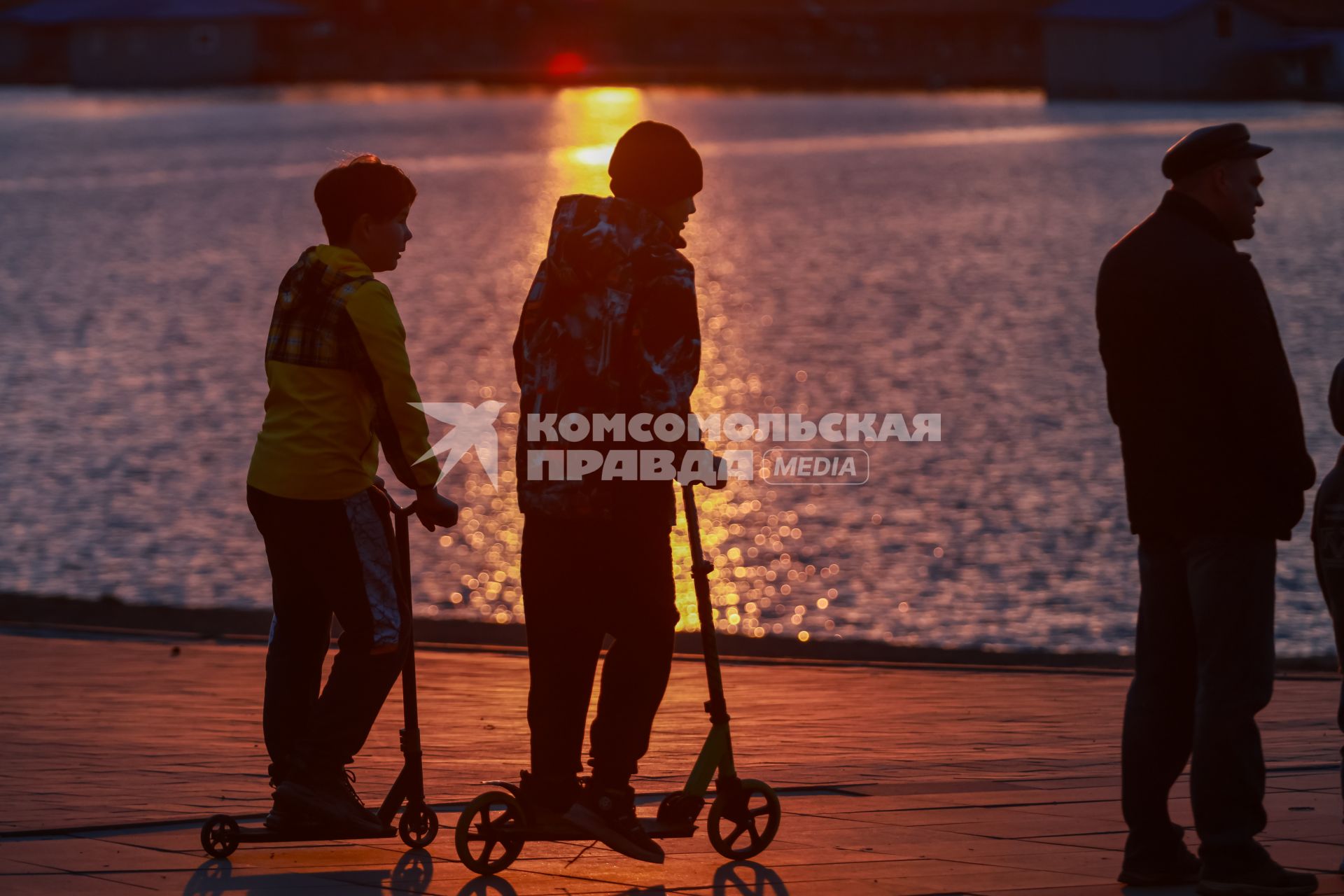 Красноярск. Подростки на самокатах на набережной во время заката.
