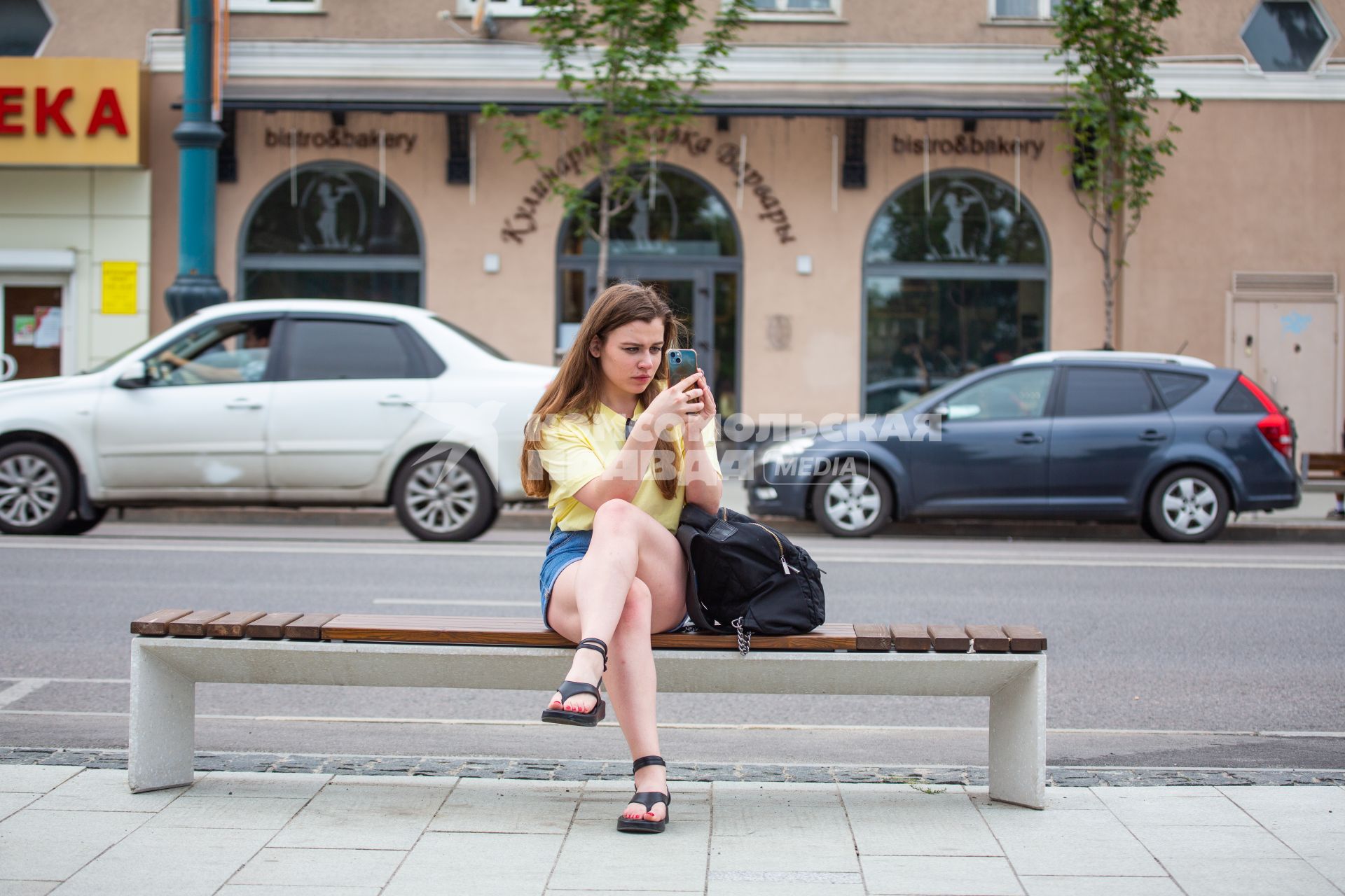 Воронеж. Девушка с мобильным телефоном сидит на лавке.
