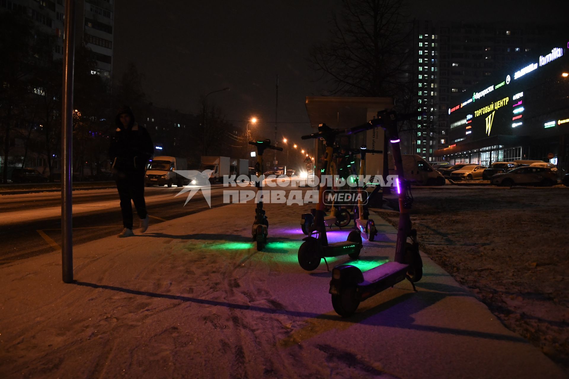 Москва. Припаркованные электросамокаты на заснеженной улице рядом с автобусной остановкой.