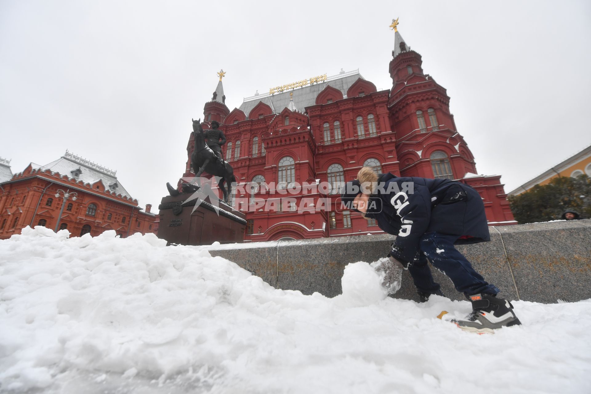 Москва. Мальчик лепит снеговика на Манежной площади у Исторического музея.