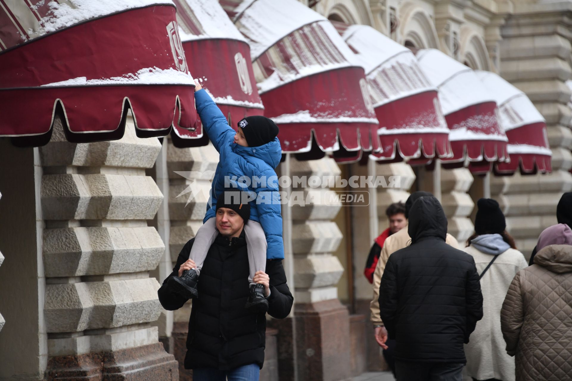 Москва. Мальчик собирает снег рукой с козырька на фасаде ГУМа, сидя у папы на шее.