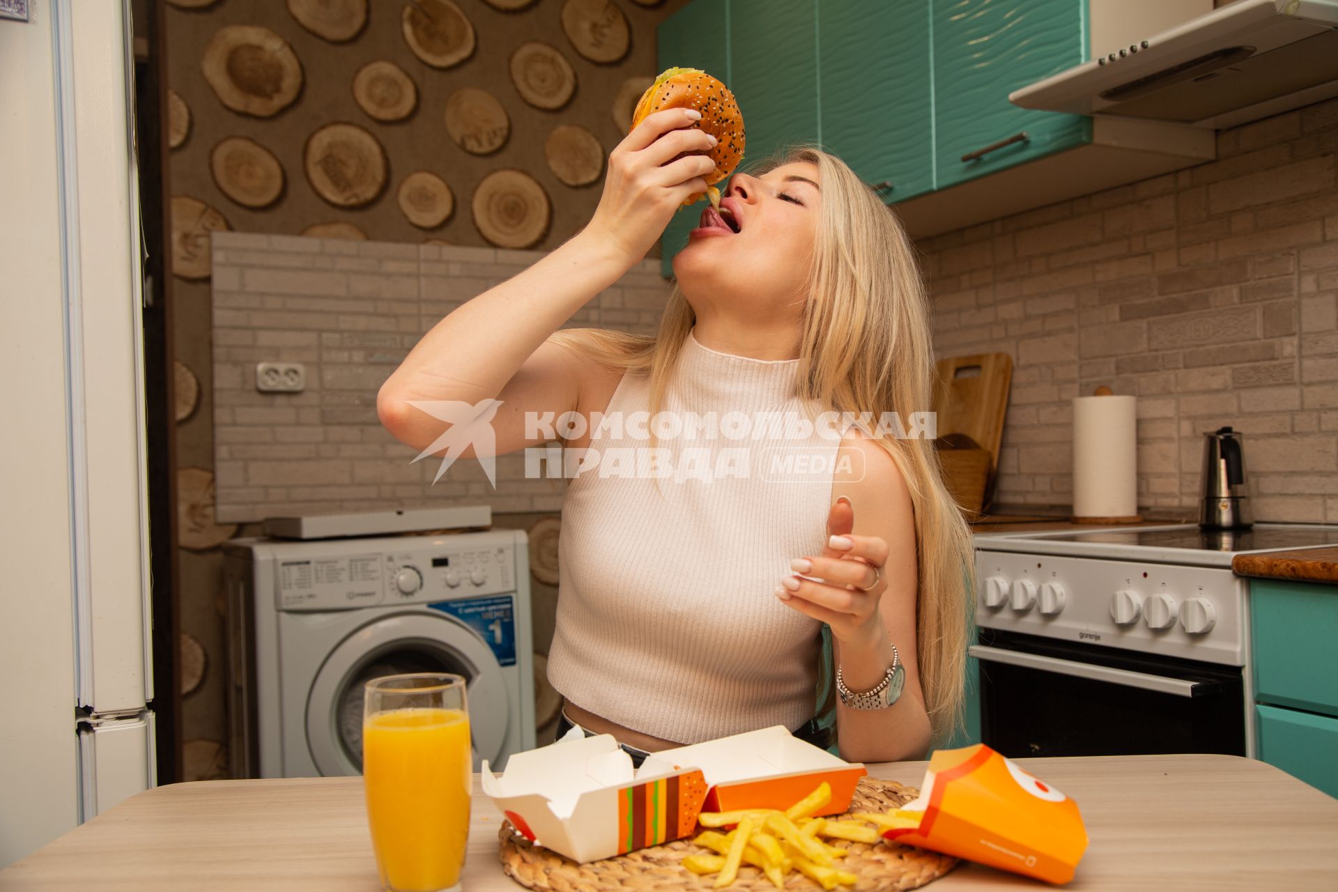 Москва.  Девушка ест гамбургер дома.