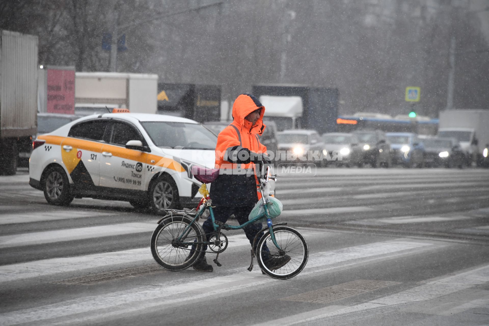 Мужчина в сигнальной куртке и с велосипедом переходит дорогу.